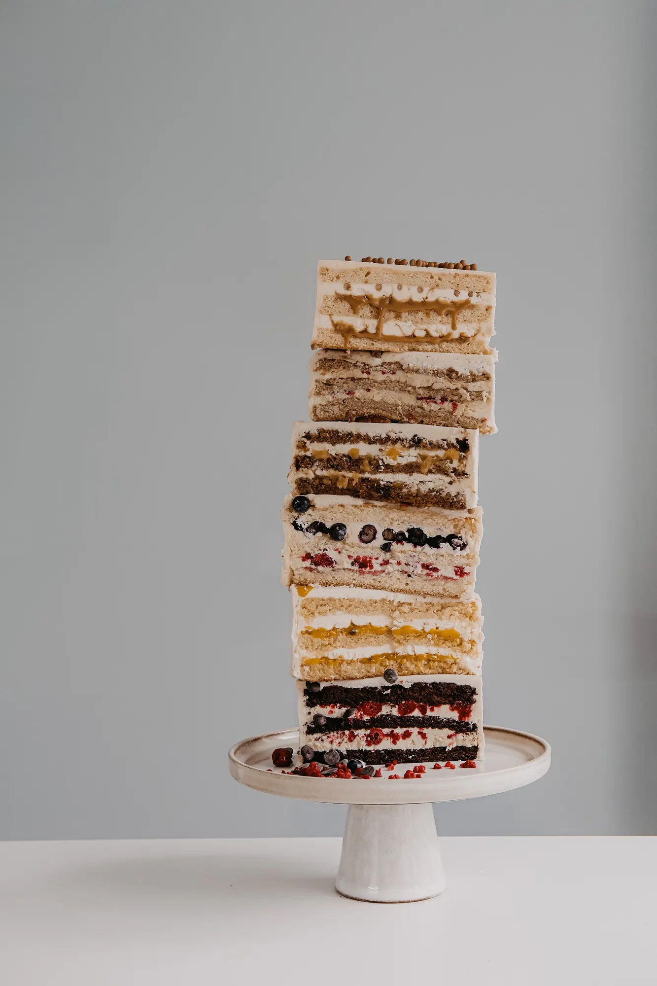 A tall stack of layered cake slices on a dark ceramic stand