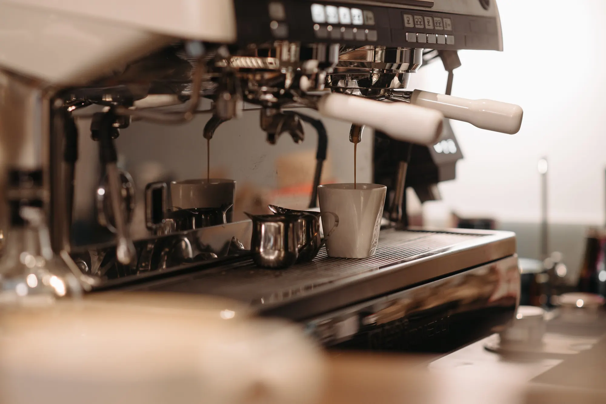 Two espressos drawing into cups on the machine, morning light behind