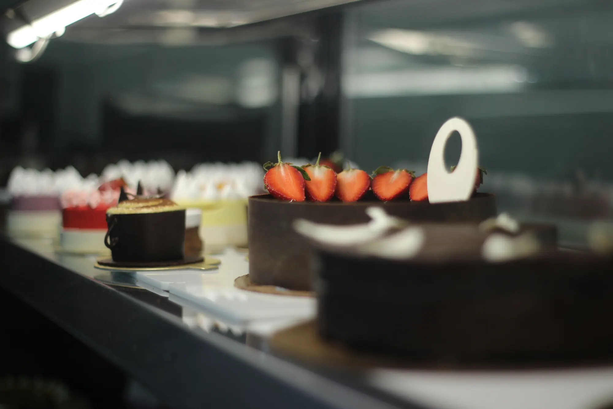Chocolate-wrapped cakes topped with fresh strawberries in a café display case