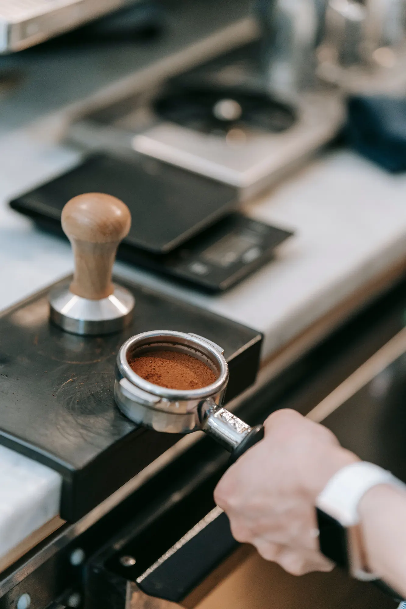 A barista levelling a portafilter of ground coffee beside a tamper