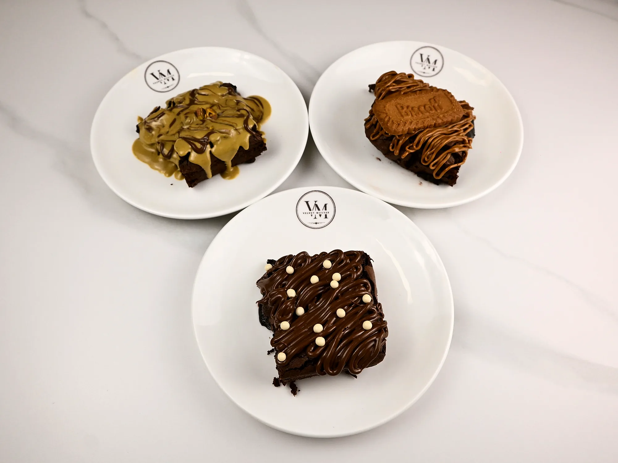 Three brownies on separate plates seen from above: pistachio, Biscoff and chocolate