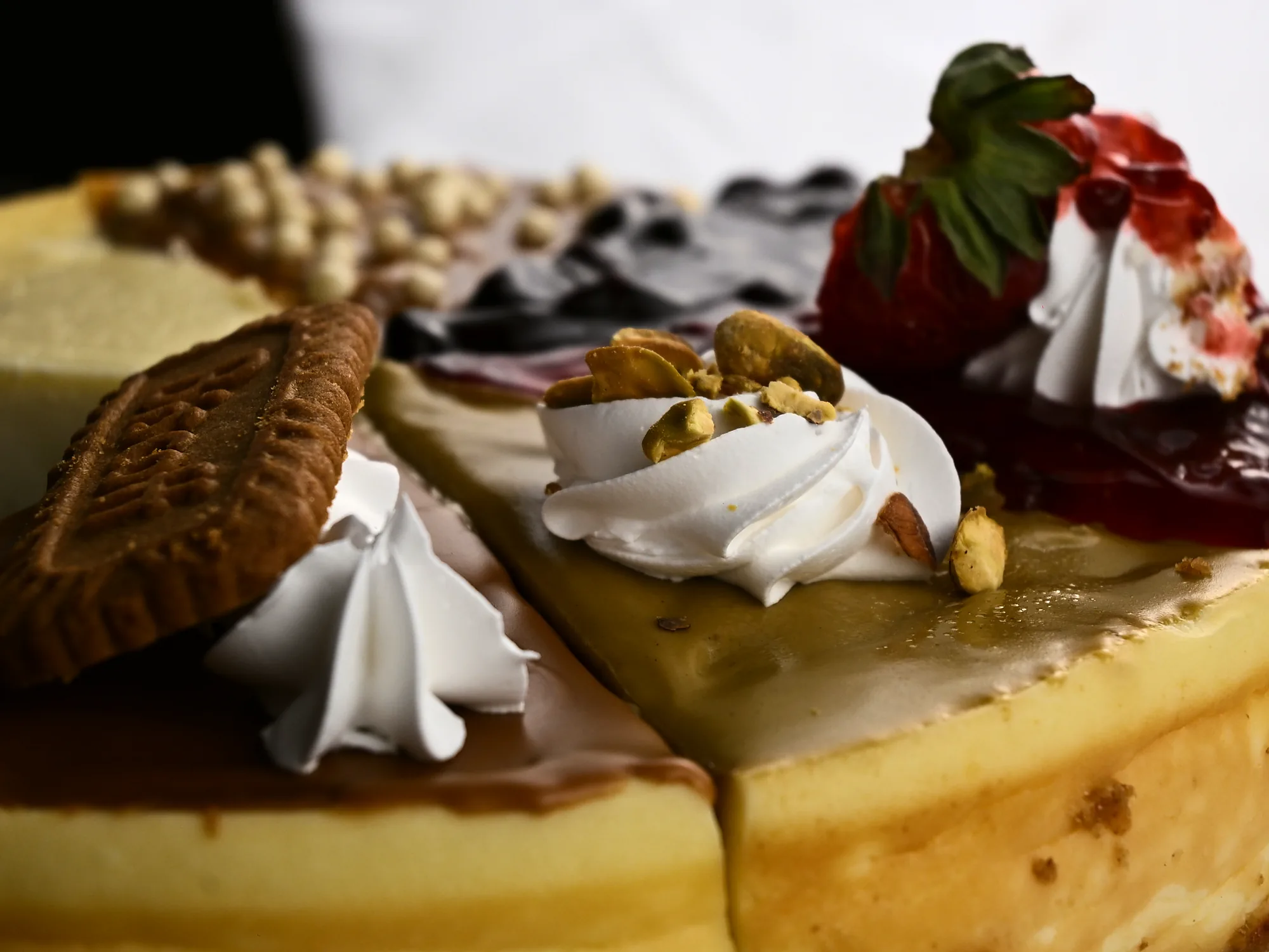 A whole cheesecake with one wedge lifted, the remaining wedges each finished differently