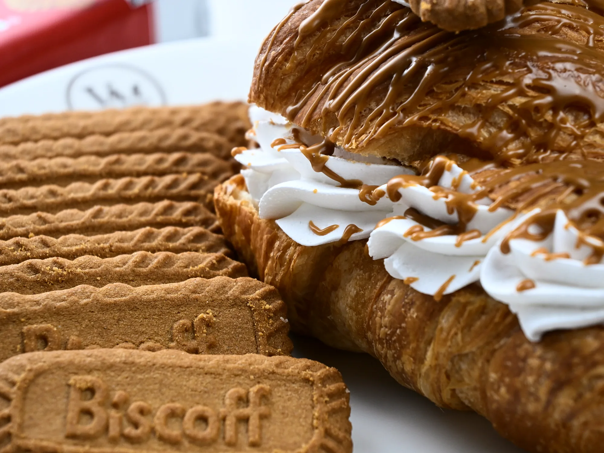 A Biscoff croissant split and piped with cream, beside stacked Biscoff biscuits
