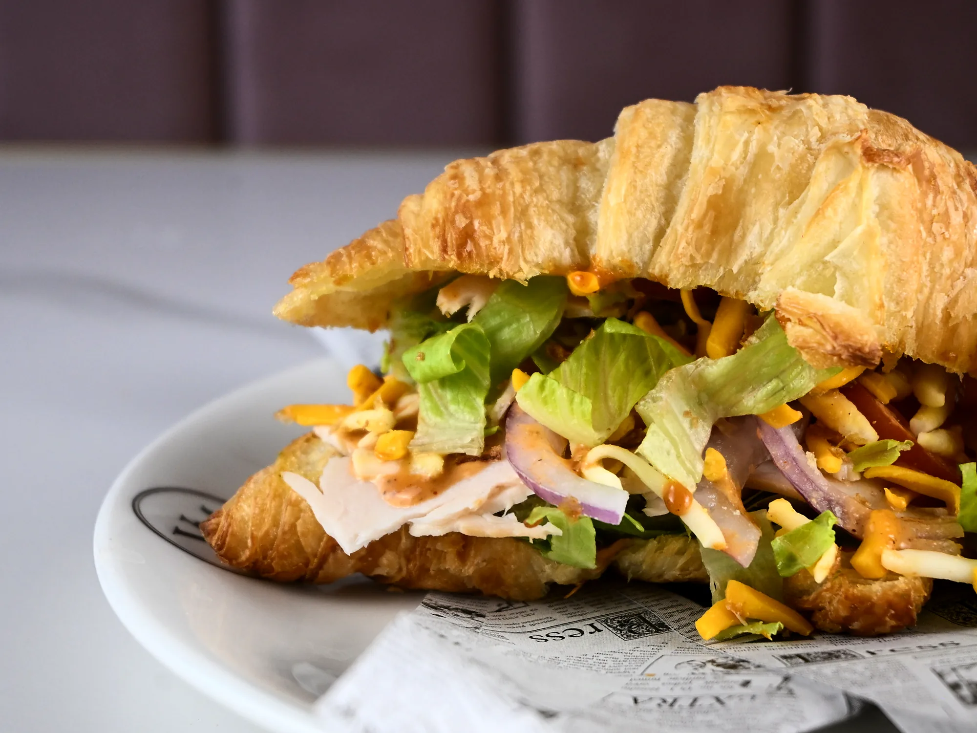 A croissant sandwich filled with turkey, cheddar, lettuce and red onion