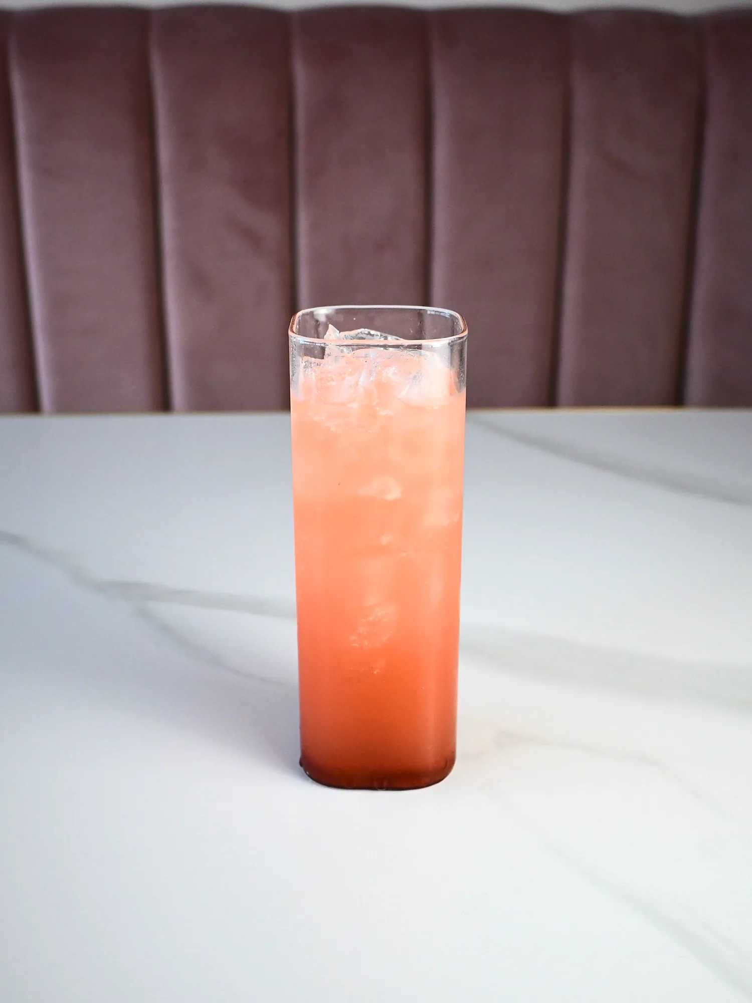 A tall glass of pink refresher over crushed ice on a marble table