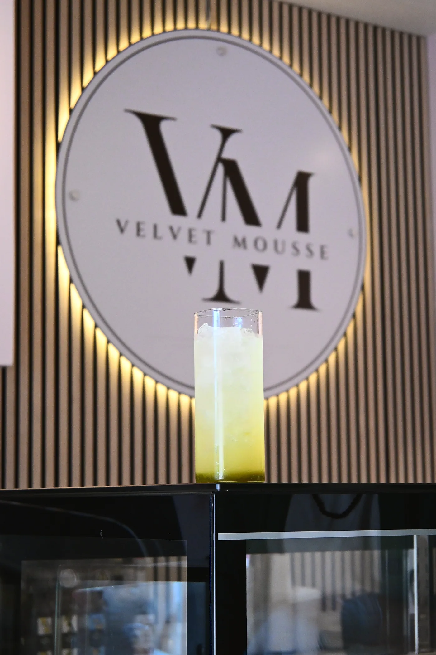 The lit Velvet Mousse roundel on the café's slatted wall above a refresher