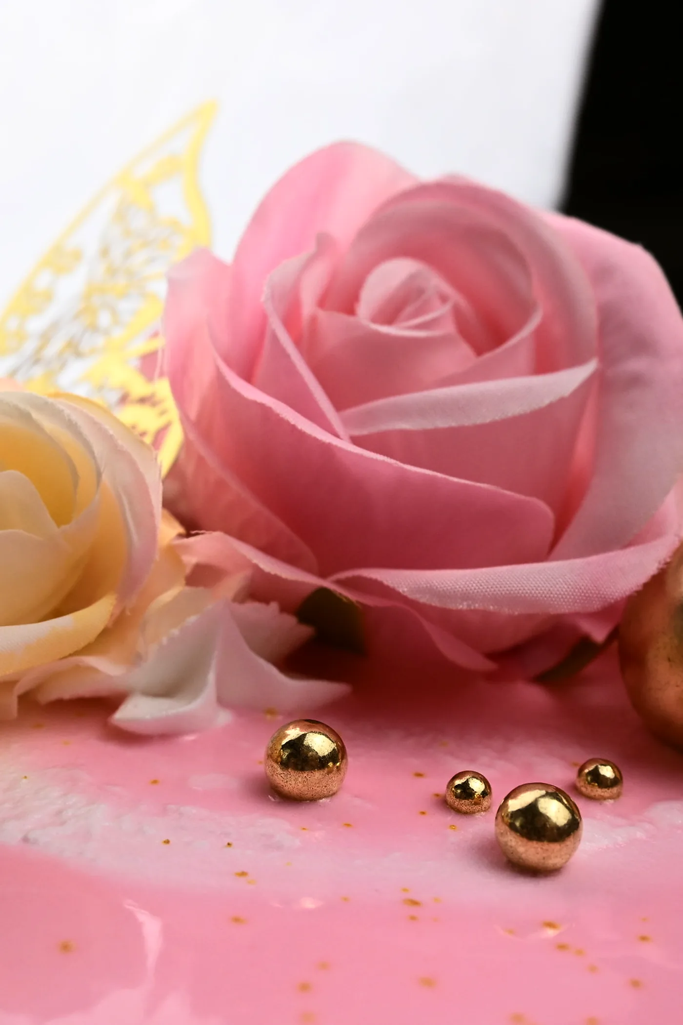 Sugar roses, gold spheres and gold leaf on the top edge of a pink celebration cake