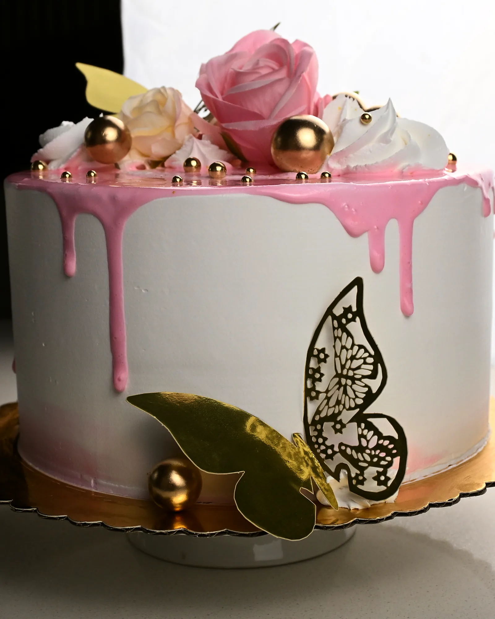 A whole celebration cake with a pink drip, sugar roses, gold spheres and a gold leaf