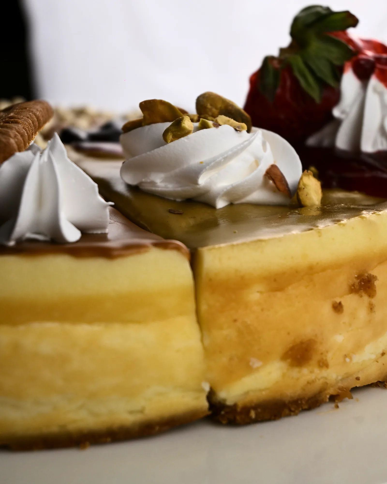 A whole baked cheesecake cut into wedges, each finished differently with pistachio, Biscoff, caramel and berries