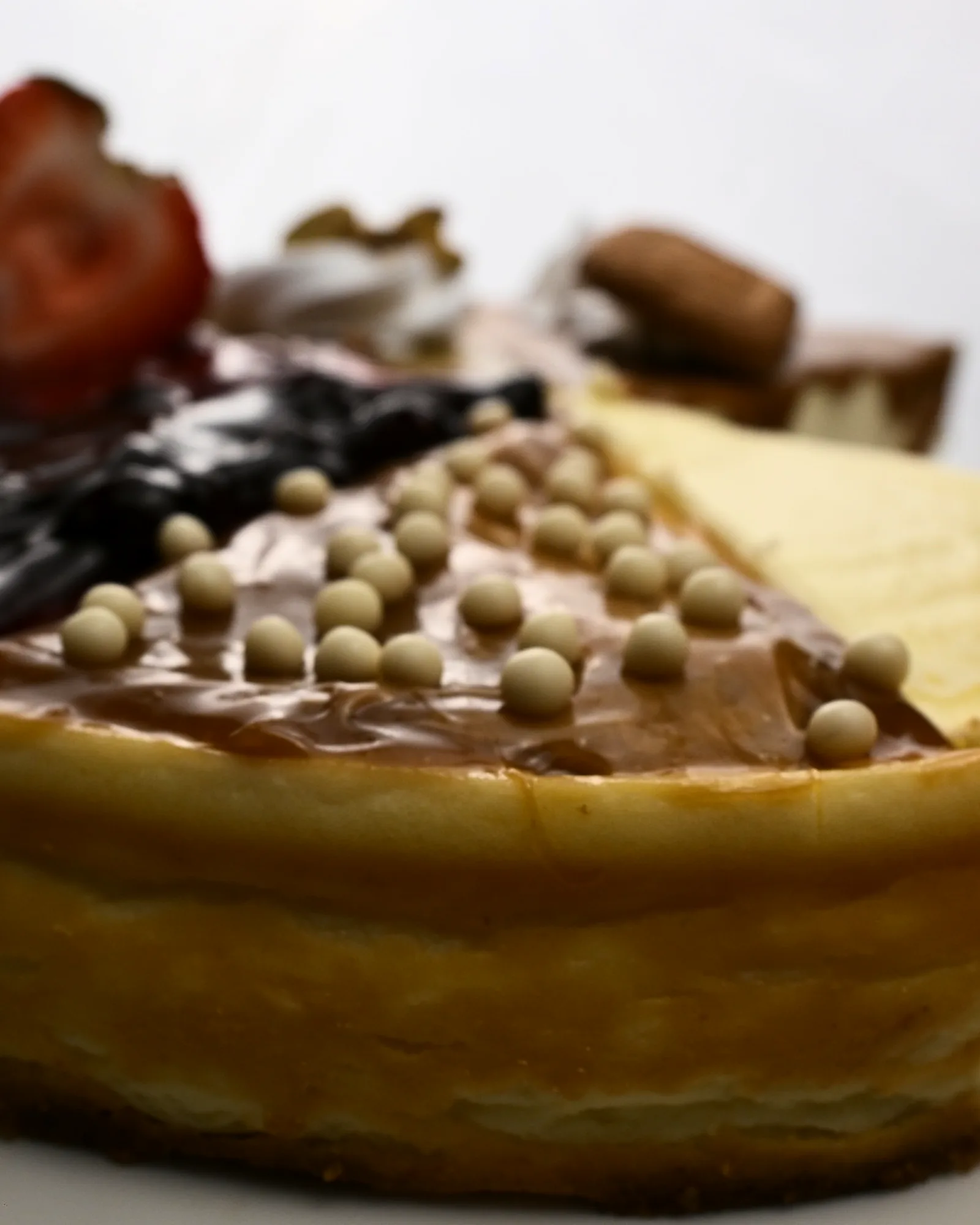 A whole baked cheesecake, its wedges finished with Biscoff, pistachio, caramel pearls and berries