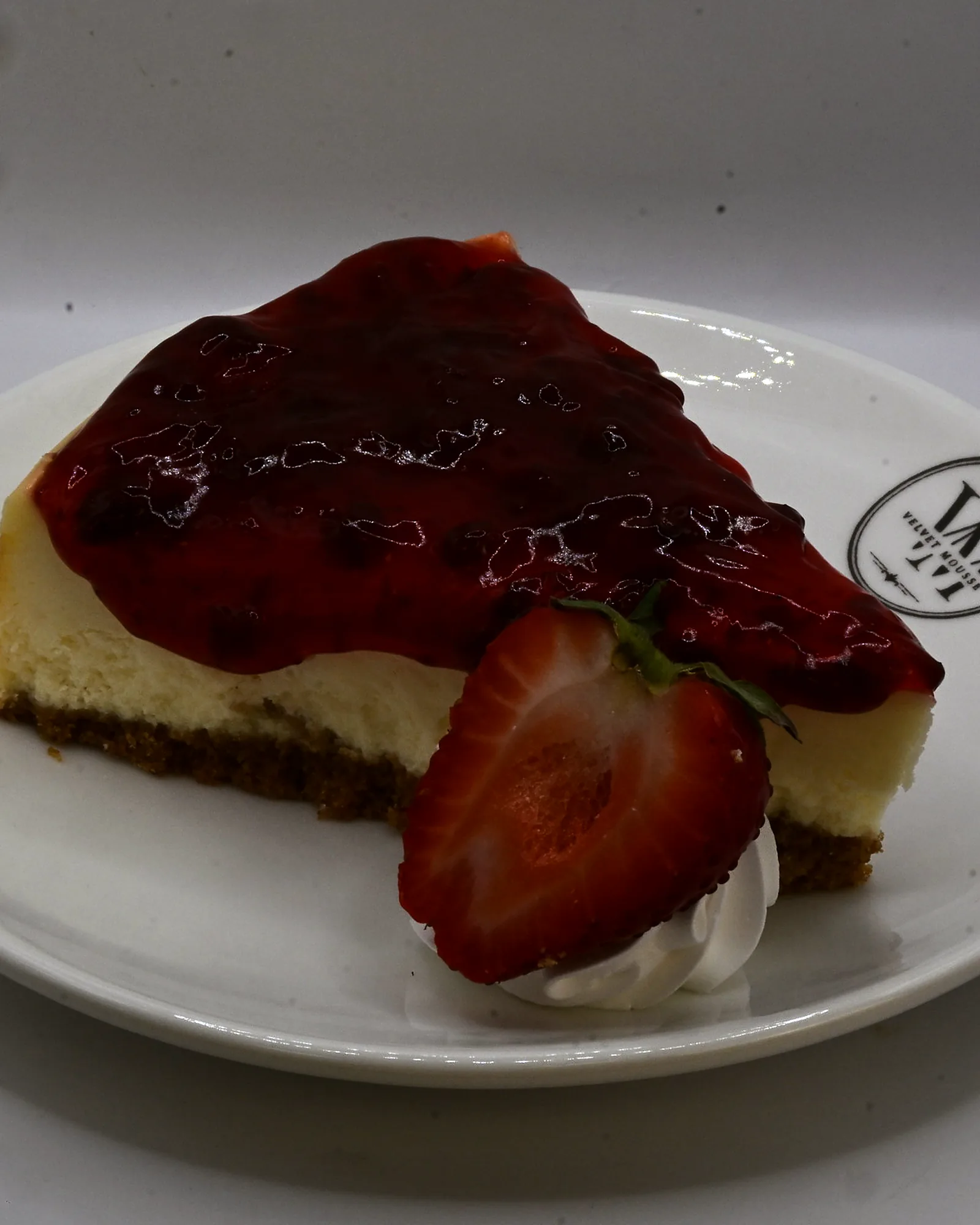 A slice of strawberry cheesecake with compote and a fresh strawberry