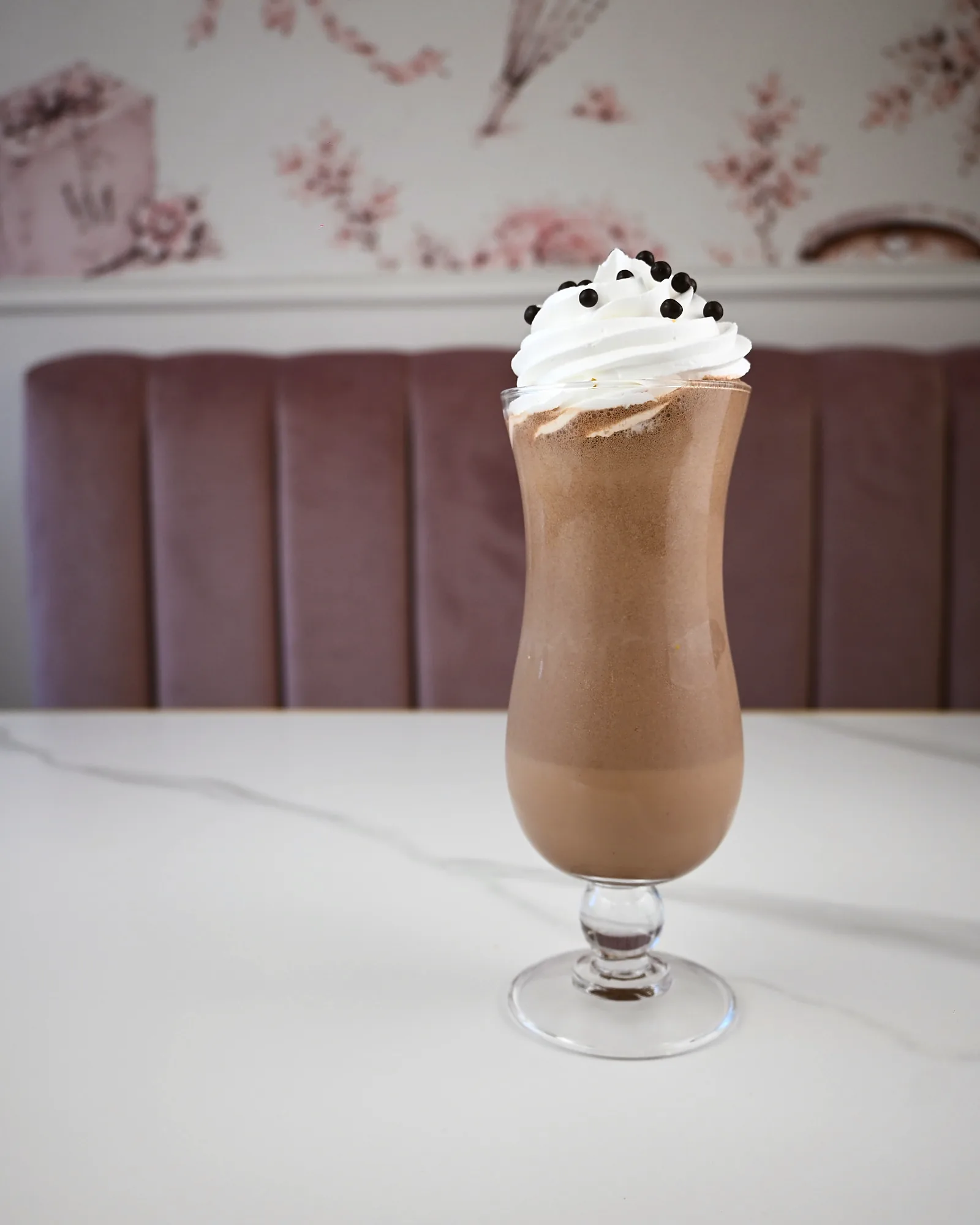 A chocolate milkshake topped with cream and cookie pieces, on the café's marble table