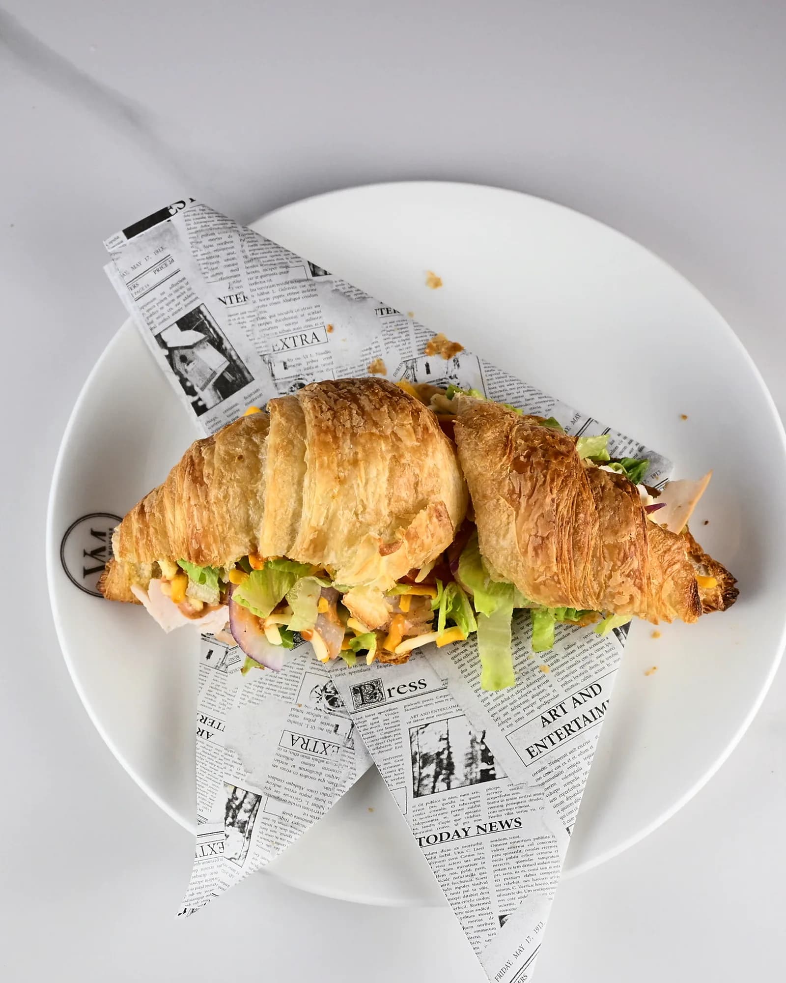 Two croissant sandwiches on a plate lined with printed paper