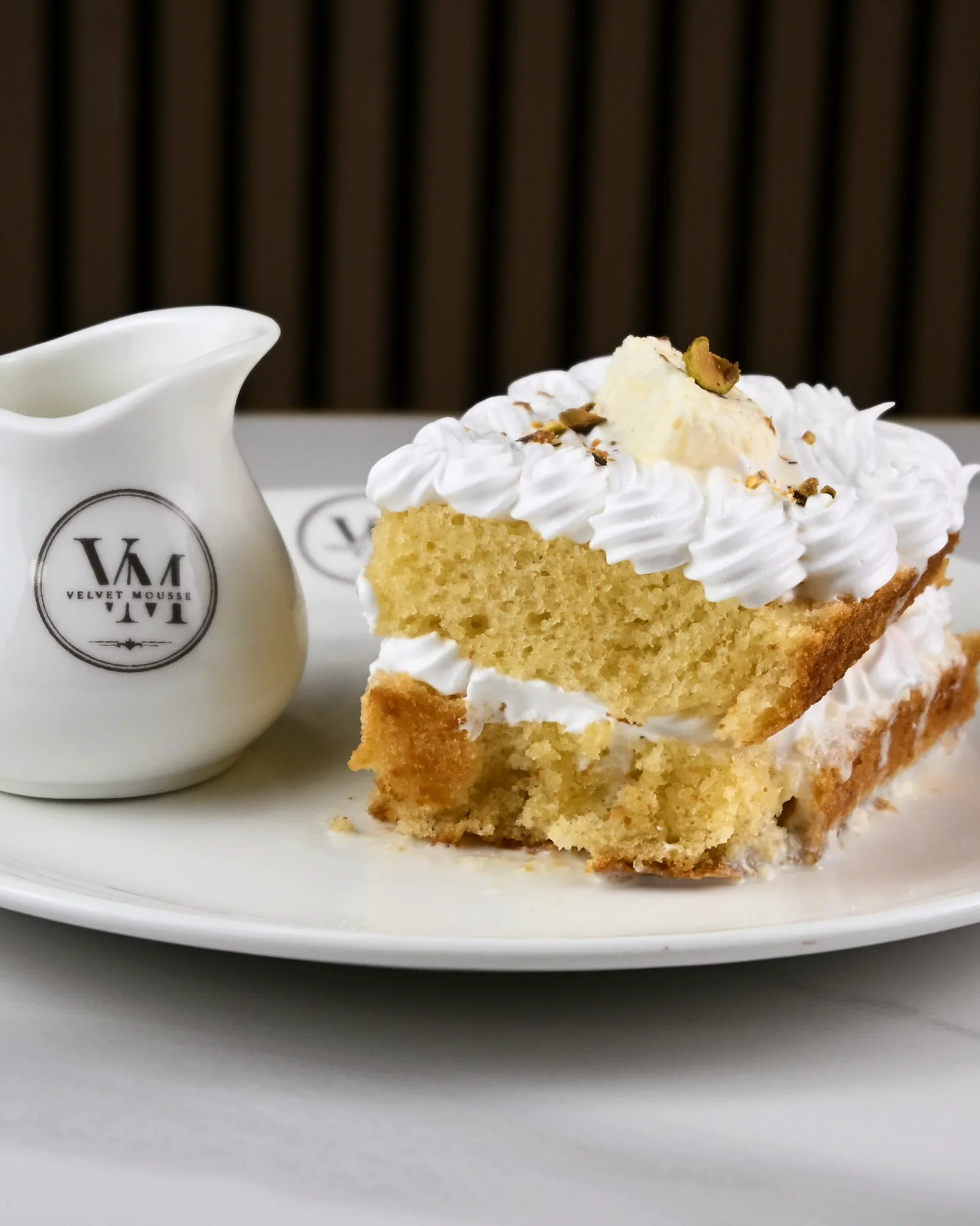 A slice of tres leches topped with cream and a strawberry, served beside a jug of milk